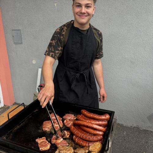 Ein Schüler beim Grillen von Fleisch und Bratwurst