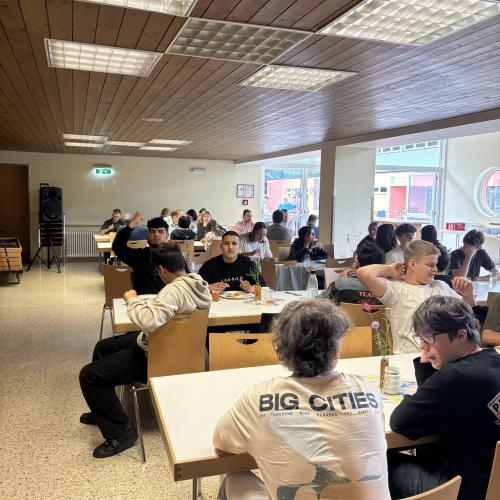 Schüler sitzen an den gedeckten Tischen. Sie essen, trinken und quatschen.