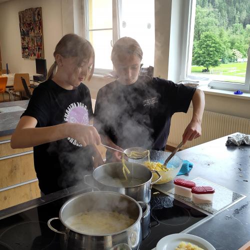 Zwei Schülerinnen am Herd, die gekochte Nudeln aus dem Topf heraus schöpfen