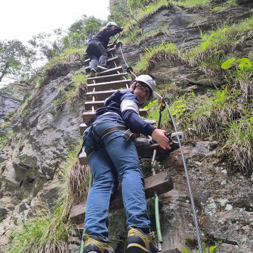 Schüler klettern an einer Holzleiter eine steile Felswand hinauf