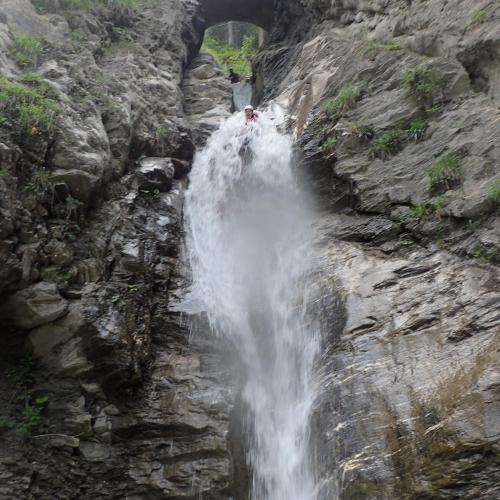 Ein Schüler rutscht einen Wasserfall am Seil hinunter, im Hintergrund eine Brücke von unten