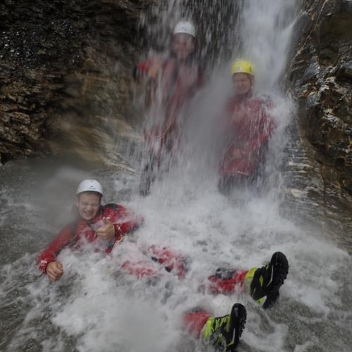 Drei Schüler:innen unterm Wasserfall, ein Schüler liegt im Wasser