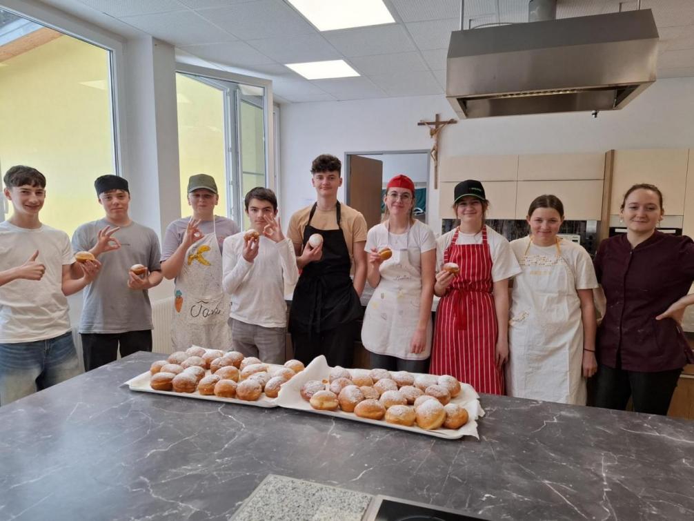 Schüler:innen Gruppe in der Küche mit Kochkleidung und im Vordergrund Platten mit selbstgemachten Krapfen