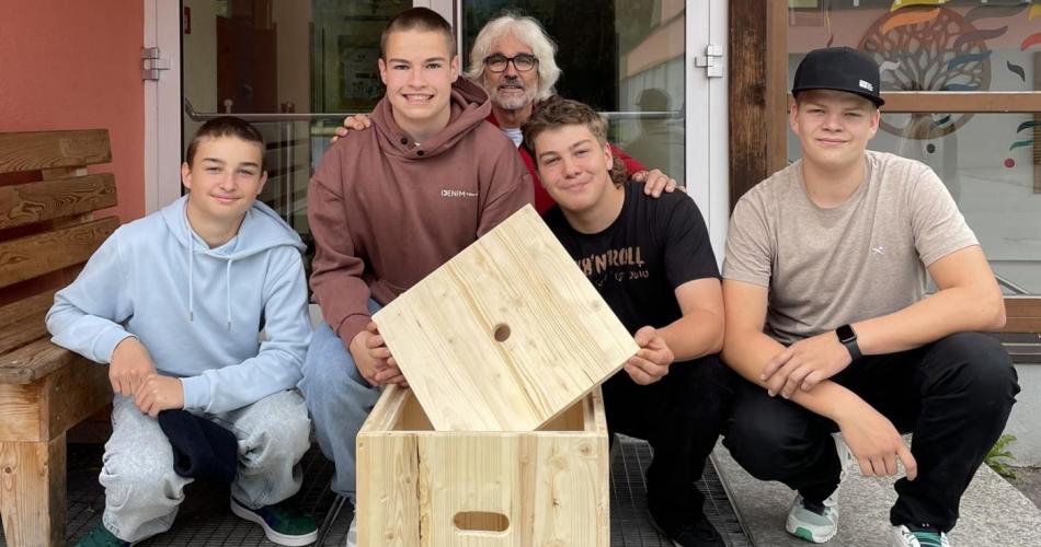 4 Schüler mit einer Lehrperson, in der Mitte ein selbstgemachter Holzhocker